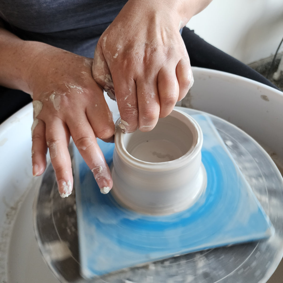 Hands shaping a clay bowl on the pottery wheel