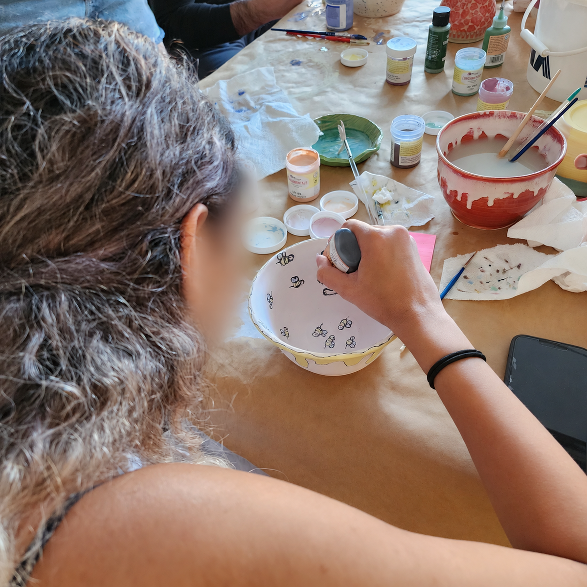 A participant painting a pottery bowl, with faces blurred