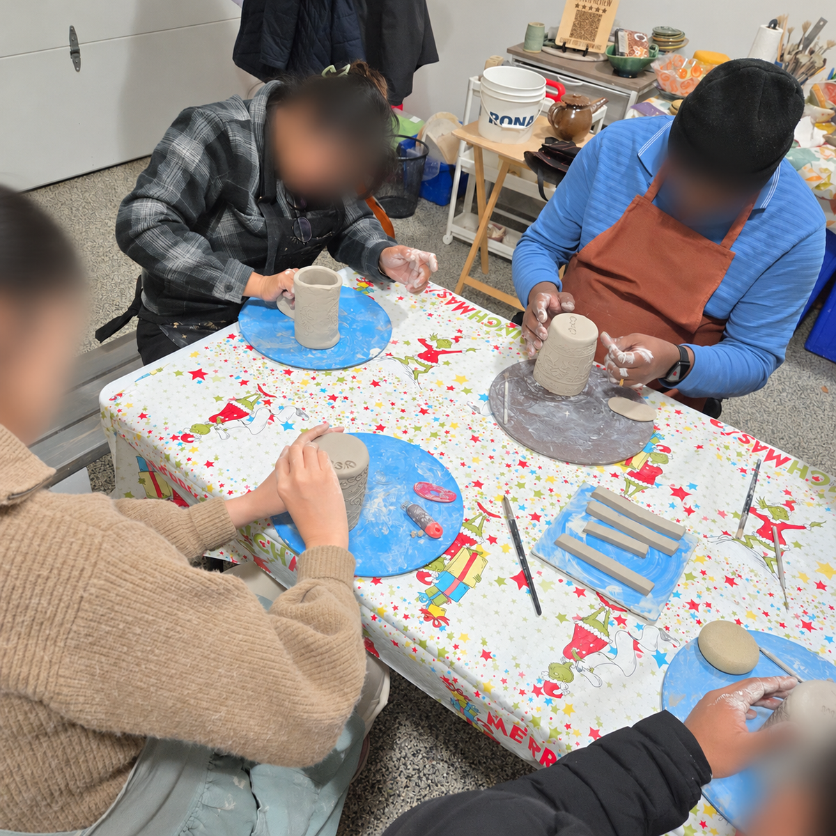 Participants painting and decorating pottery together, with faces blurred