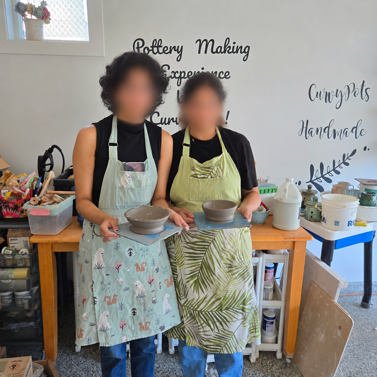 Two participants with their handmade bowls after a pottery wheel throwing workshop, with faces blurred